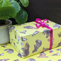 Gift wrapped in yellow paper with animal pattern and pink ribbon, next to a potted plant.